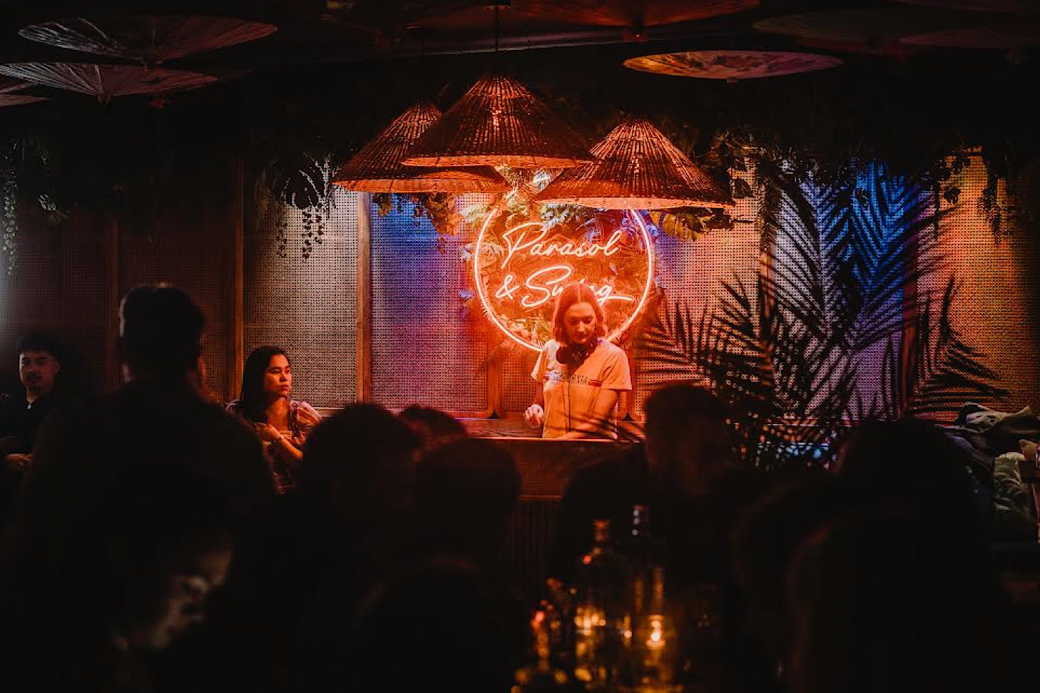 A DJ plays a set in front of an orange neon wall decal of the words Parasol and Swing.